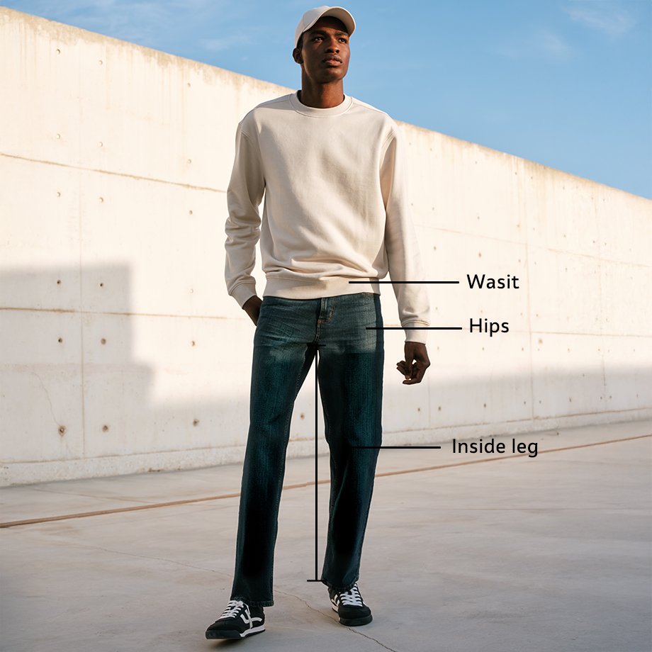 Person wearing a cream knit sweater and blue straight-leg jeans with white sneakers, showing waist and inside leg measurement guides.